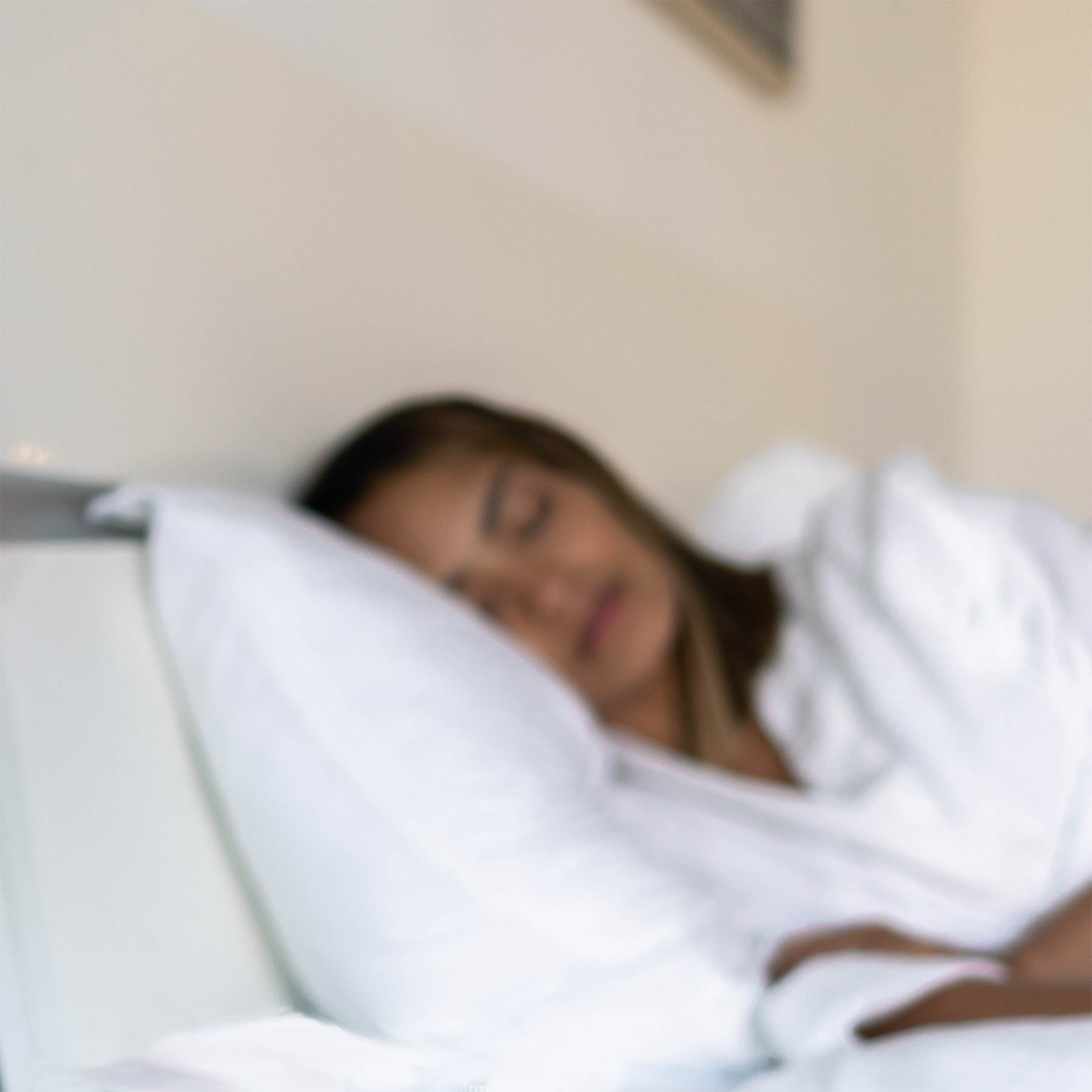 Image of woman sleeping in bed on her side facing the camera, looking restful.